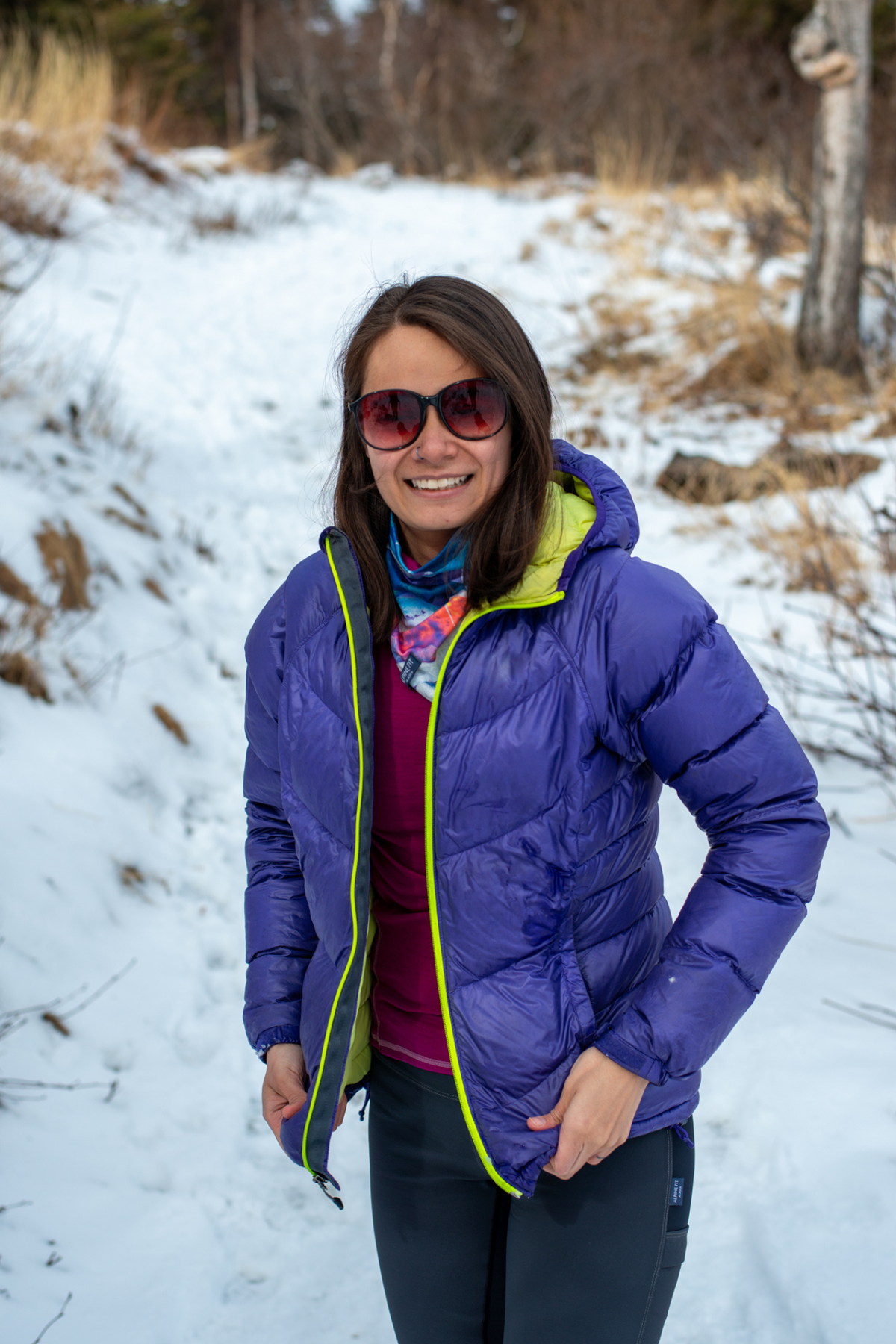 Alpine Fit Mountain V Fleece Neck Warmer Sunrise, Woman in a purple jacket standing in a snowy landscape