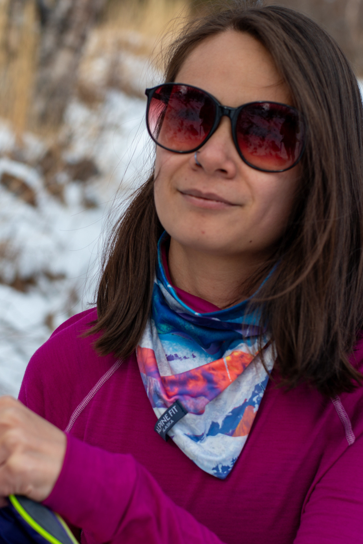 Alpine Fit Mountain V Merino Wool Neck Warmer Sunrise, Woman wearing sunglasses and a colorful neck warmer in a snowy outdoor setting