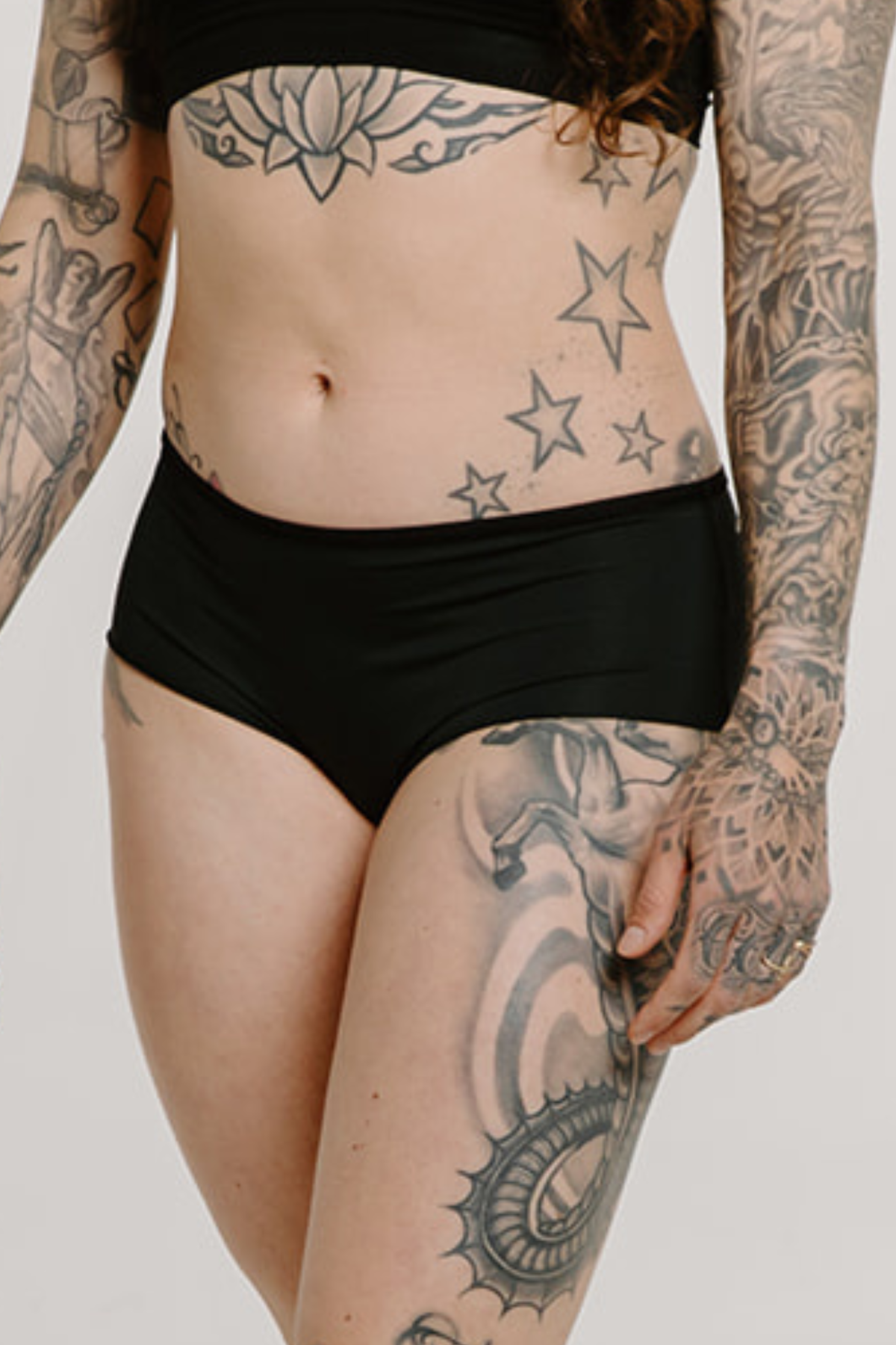 Alpine Fit Athletic Hipster Black, Person wearing black underwear with visible tattoos on arms and legs against a neutral background